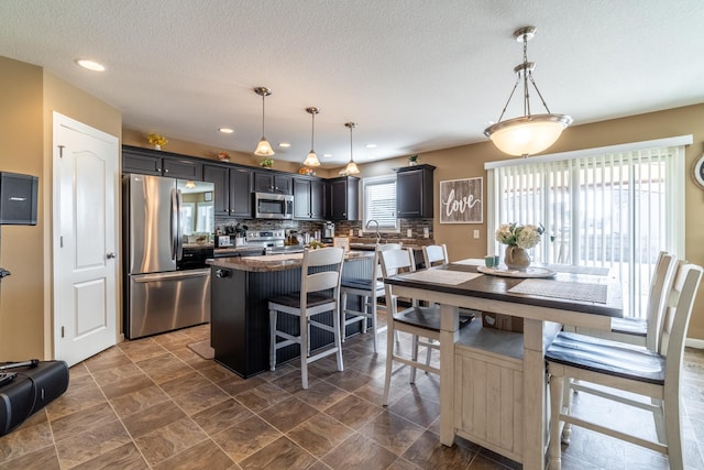 kitchen with a breakfast bar area, stainless steel appliances, hanging light fixtures, backsplash, and a center island