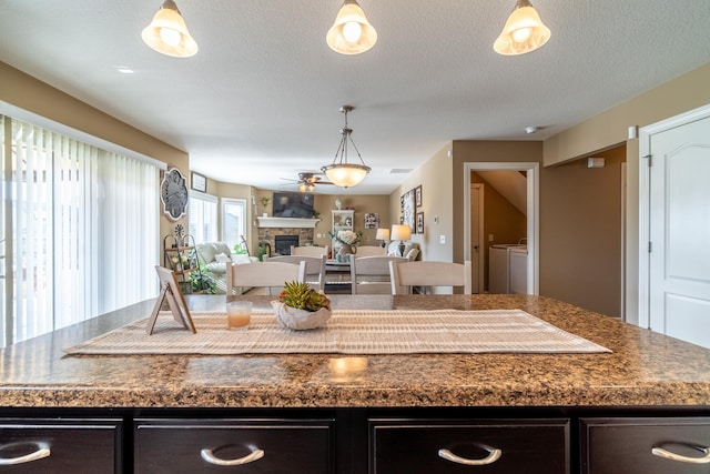 kitchen with a stone fireplace, dark countertops, washing machine and clothes dryer, and a center island