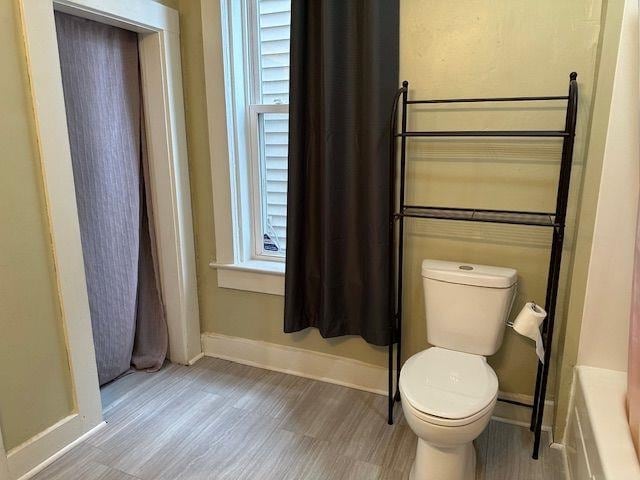 bathroom with a bathing tub, baseboards, toilet, and wood finished floors