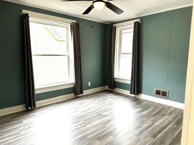 spare room with baseboards, wood finished floors, visible vents, and crown molding