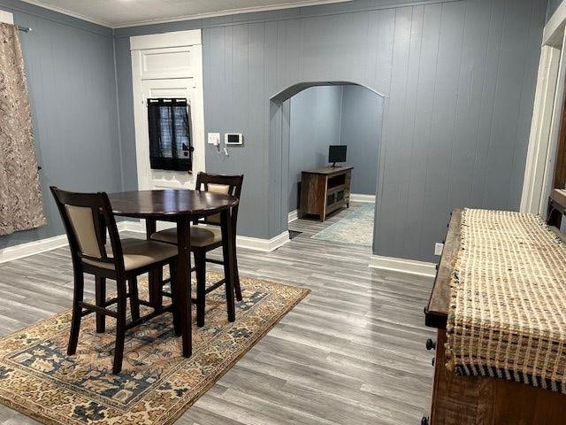 dining area featuring arched walkways, crown molding, baseboards, and light wood-style floors