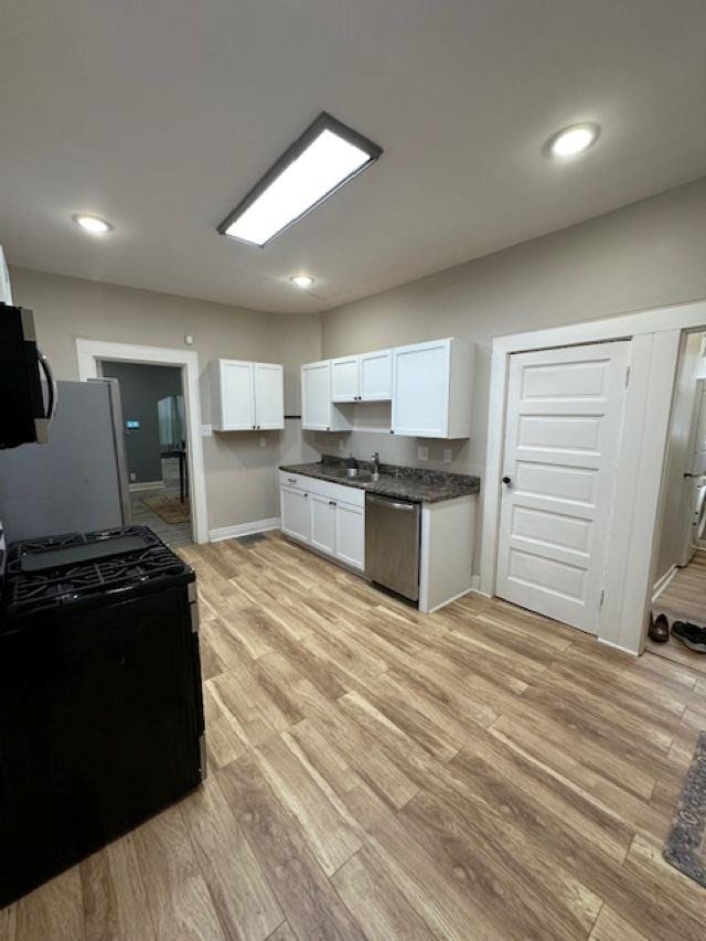 kitchen featuring stainless steel appliances, dark countertops, white cabinetry, a sink, and light wood-type flooring