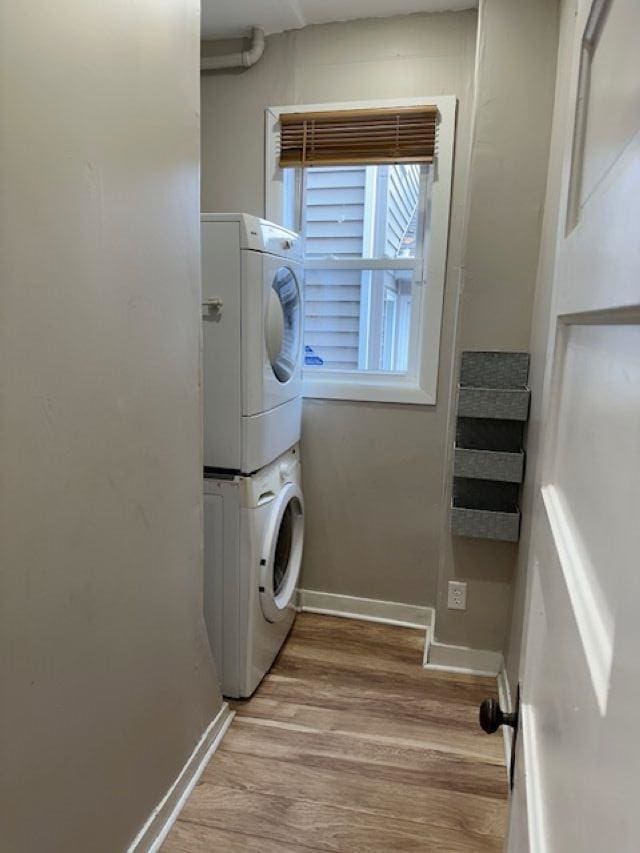 washroom with light wood-type flooring, laundry area, baseboards, and stacked washer / dryer