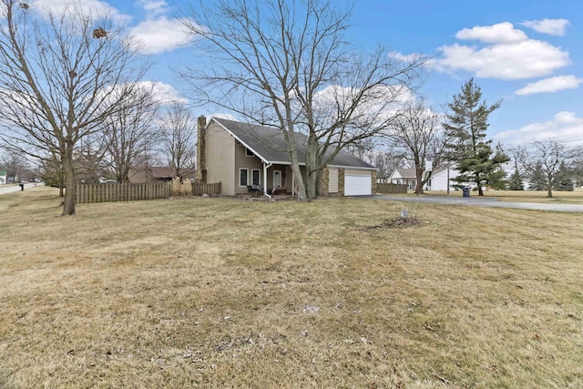 exterior space with a chimney, aphalt driveway, an attached garage, fence, and a front yard