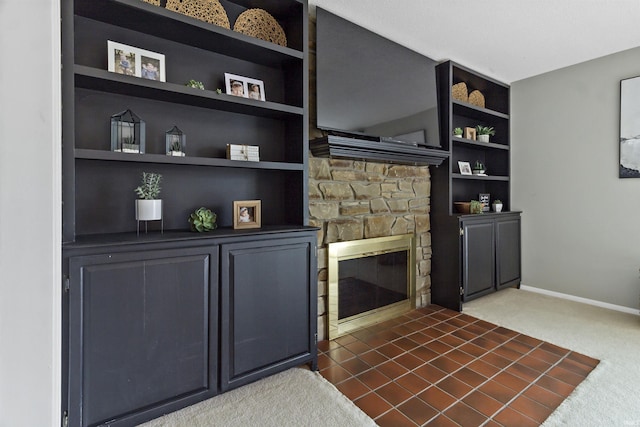 living area featuring baseboards, dark carpet, built in features, and a stone fireplace