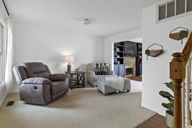 living area with baseboards, built in shelves, visible vents, and a stone fireplace