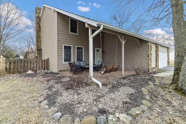 back of house with fence, a chimney, an attached garage, and an outdoor hangout area