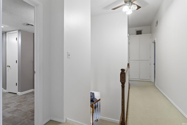 corridor featuring visible vents, a textured ceiling, an upstairs landing, and baseboards