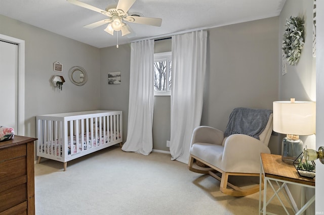 bedroom with carpet, ceiling fan, and a crib