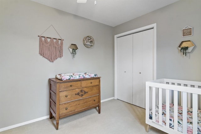 carpeted bedroom featuring a nursery area, ceiling fan, a closet, and baseboards