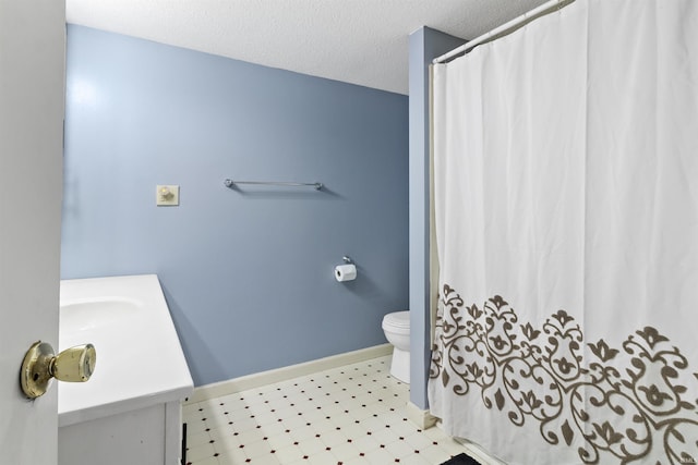 bathroom with a textured ceiling, curtained shower, toilet, vanity, and baseboards