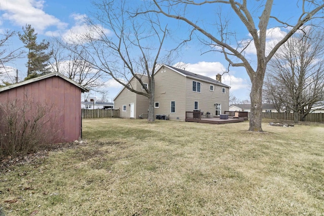 rear view of property featuring an outbuilding, a chimney, a lawn, fence, and a wooden deck