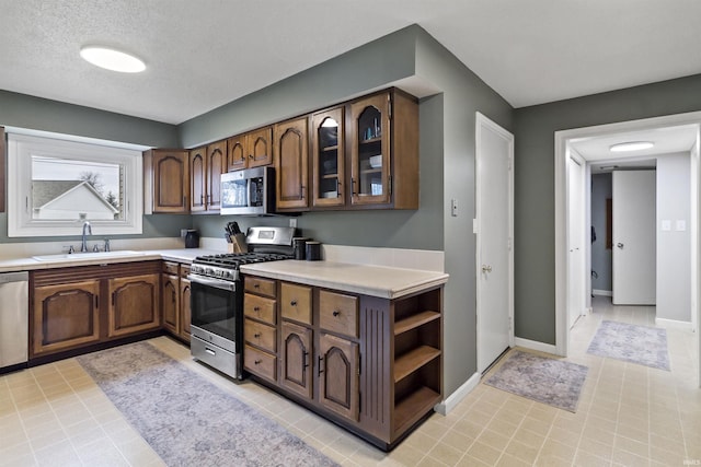 kitchen with baseboards, glass insert cabinets, appliances with stainless steel finishes, light countertops, and a sink