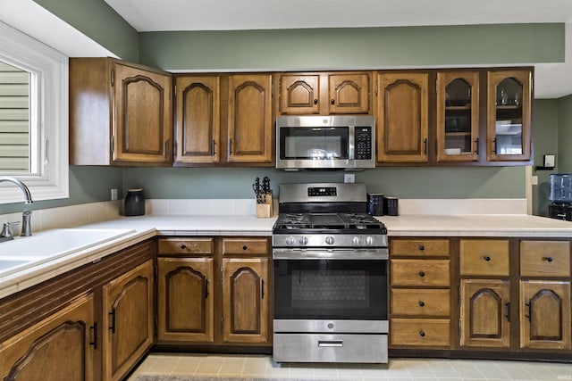 kitchen featuring tile countertops, stainless steel appliances, brown cabinetry, and a sink