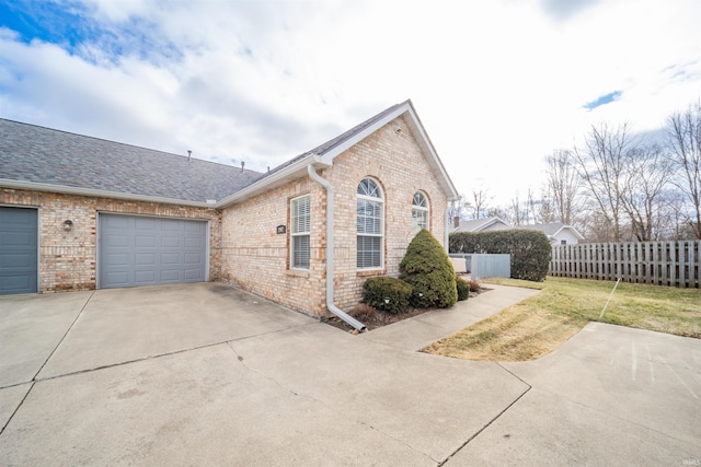 view of home's exterior featuring a garage, concrete driveway, brick siding, and fence