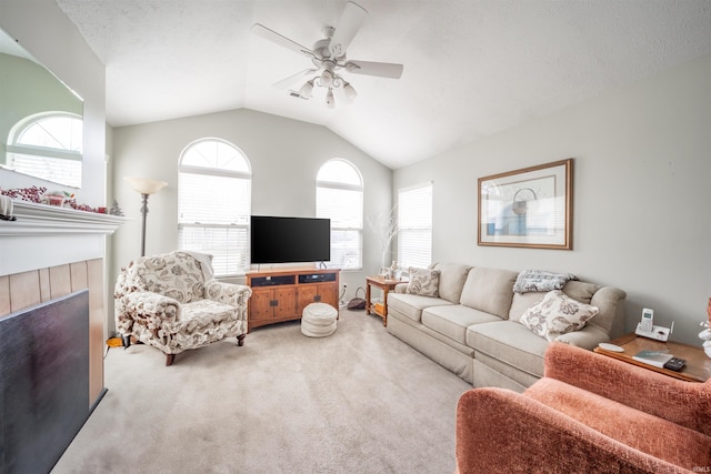 living room with a ceiling fan, a tiled fireplace, lofted ceiling, light colored carpet, and a textured ceiling