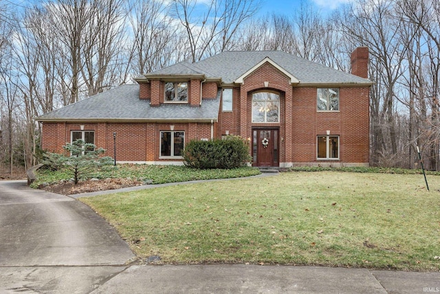 view of front facade with roof with shingles, a chimney, a front lawn, and brick siding