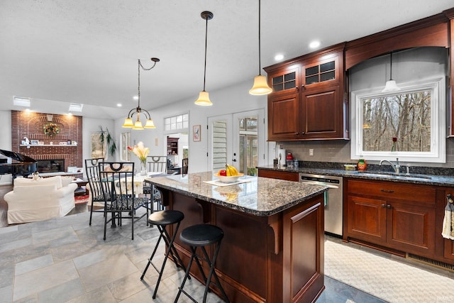 kitchen with a sink, hanging light fixtures, a brick fireplace, a center island, and dishwasher