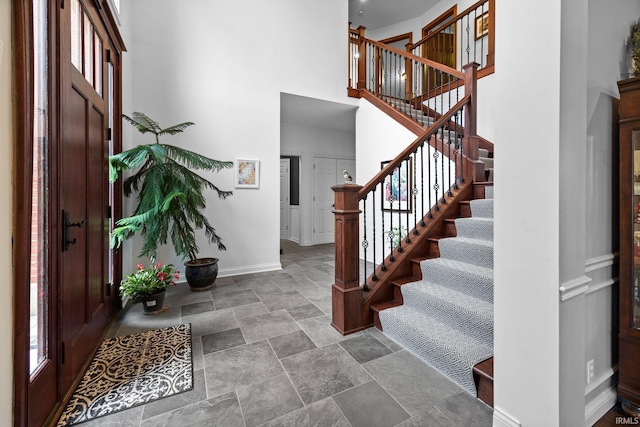 entrance foyer featuring stairway, stone finish flooring, a towering ceiling, and baseboards