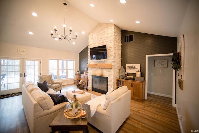 living room with a stone fireplace, a notable chandelier, wood finished floors, visible vents, and french doors