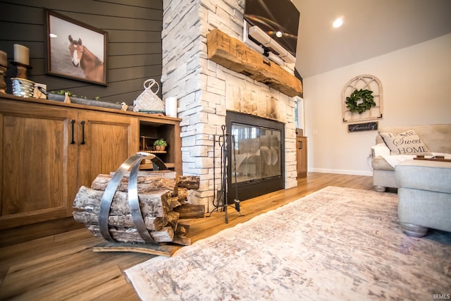 living room with lofted ceiling, baseboards, wood finished floors, and a stone fireplace