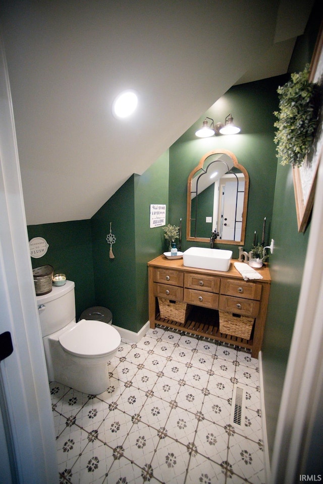 half bathroom with baseboards, vaulted ceiling, vanity, and toilet