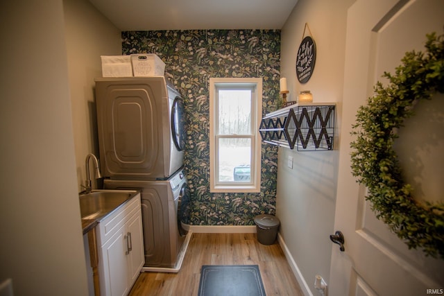 washroom with baseboards, light wood-type flooring, stacked washing maching and dryer, cabinet space, and wallpapered walls