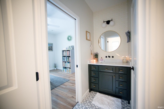 bathroom with an accent wall, wood finished floors, vanity, baseboards, and wallpapered walls