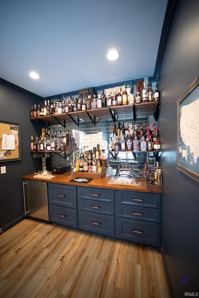 bar featuring backsplash, light wood-style floors, ornamental molding, bar area, and fridge