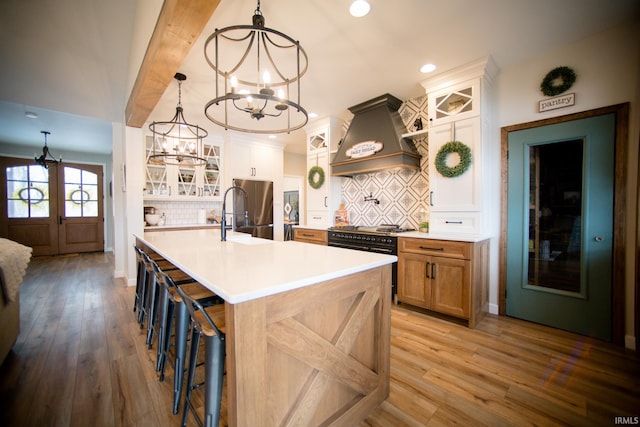 kitchen featuring a chandelier, freestanding refrigerator, premium range hood, and light wood-style flooring