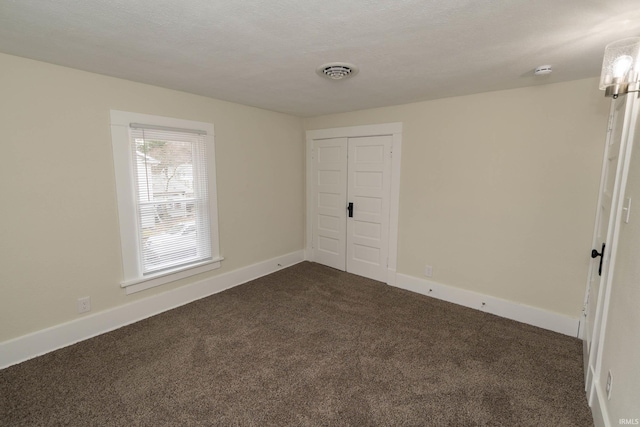 empty room with dark colored carpet, visible vents, a textured ceiling, and baseboards