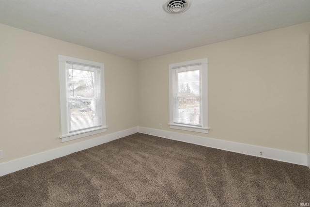 spare room with baseboards, dark carpet, visible vents, and a healthy amount of sunlight