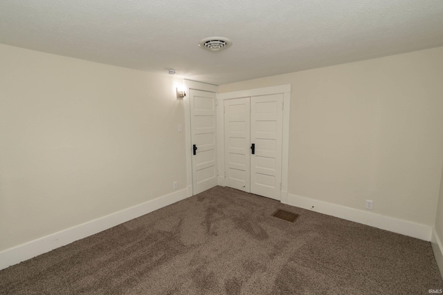 spare room with dark colored carpet, visible vents, and baseboards