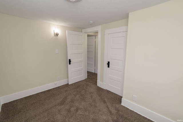 empty room featuring baseboards and dark colored carpet