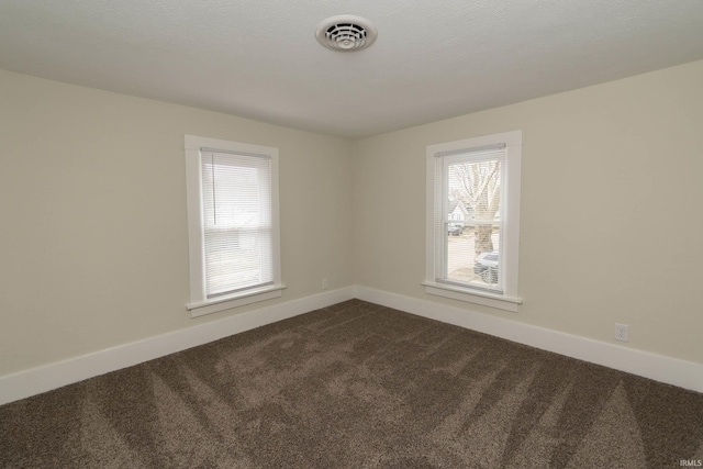 spare room with dark colored carpet, visible vents, a textured ceiling, and baseboards