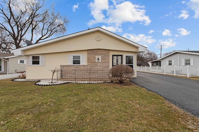 view of front facade with stone siding, fence, aphalt driveway, and a front yard