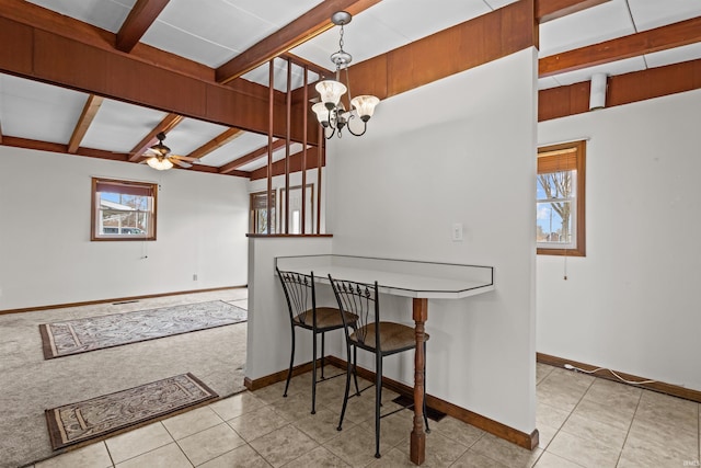 tiled dining room with ceiling fan with notable chandelier, carpet floors, beamed ceiling, and baseboards