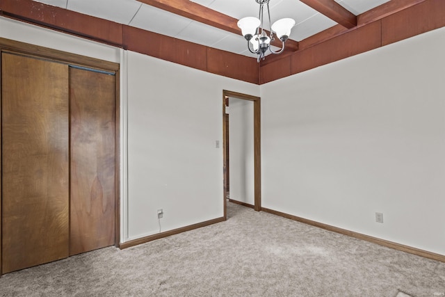 unfurnished bedroom with beam ceiling, a notable chandelier, a closet, carpet flooring, and baseboards