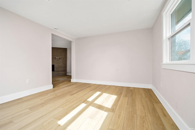 spare room with light wood finished floors, a brick fireplace, and baseboards