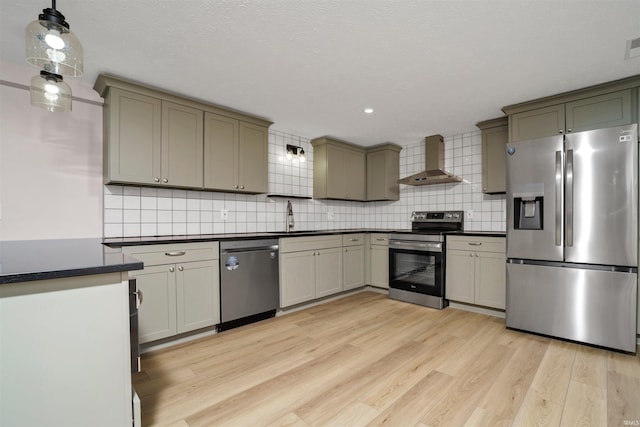 kitchen featuring dark countertops, wall chimney exhaust hood, appliances with stainless steel finishes, light wood-type flooring, and a sink