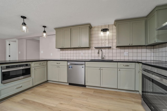 kitchen featuring tasteful backsplash, dark countertops, stainless steel appliances, light wood-type flooring, and a sink