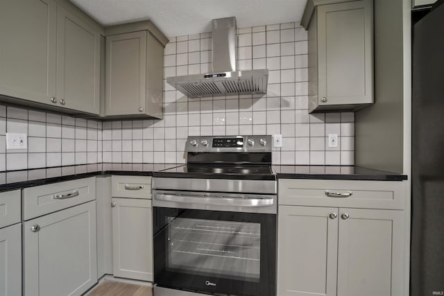 kitchen featuring stainless steel electric stove, dark countertops, decorative backsplash, gray cabinetry, and wall chimney exhaust hood