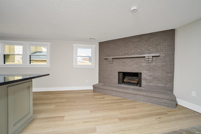 unfurnished living room with a brick fireplace, light wood-style flooring, baseboards, and a textured ceiling