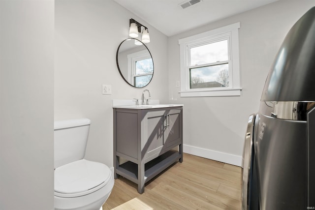 half bath with baseboards, visible vents, toilet, wood finished floors, and vanity