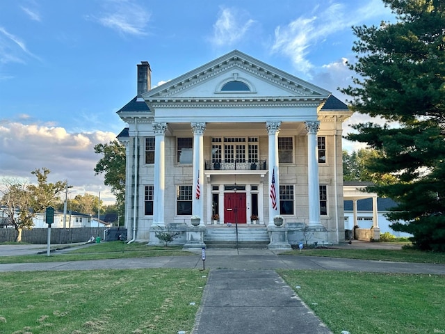 neoclassical home with a porch, a chimney, a front yard, and a balcony