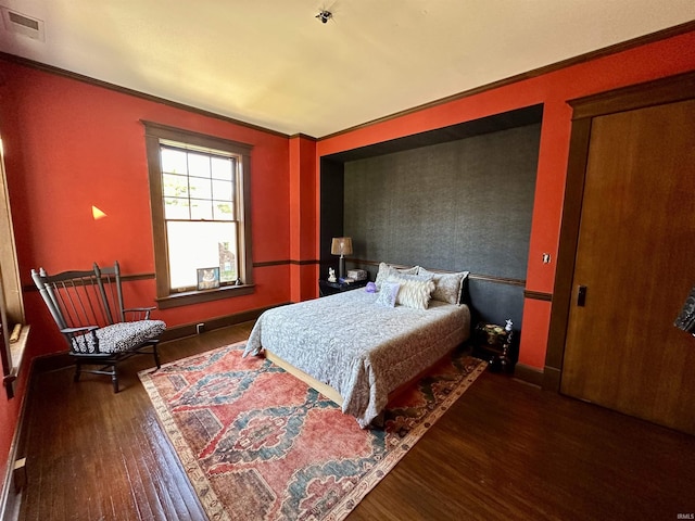 bedroom with ornamental molding, visible vents, baseboards, and wood finished floors