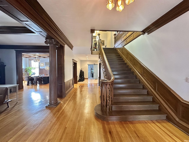 stairway with ornate columns, wood finished floors, a notable chandelier, and wainscoting