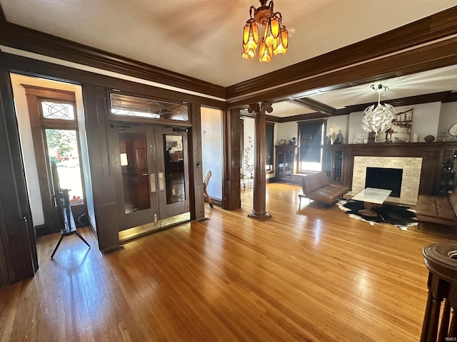 living room featuring decorative columns, a fireplace, crown molding, and wood finished floors