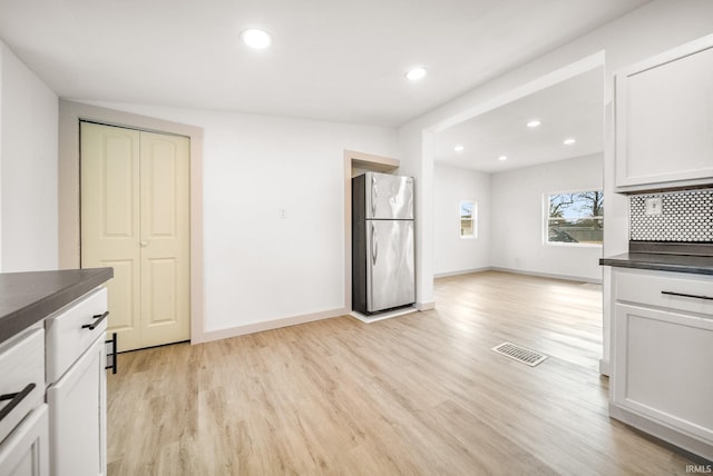 kitchen with visible vents, dark countertops, freestanding refrigerator, light wood-type flooring, and backsplash