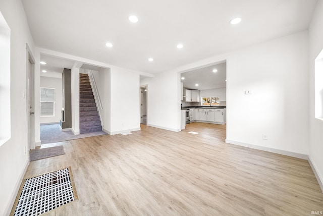 unfurnished living room featuring recessed lighting, baseboards, light wood finished floors, and stairs